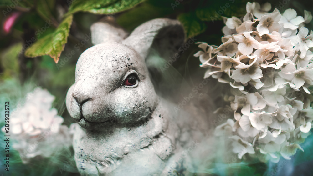 Stone rabbit hide in a bouquet of white viburnum in the garden / forest