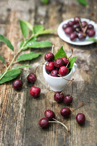 cherry berries in raindrops lie in a mug on a wooden table against a background of greenery
