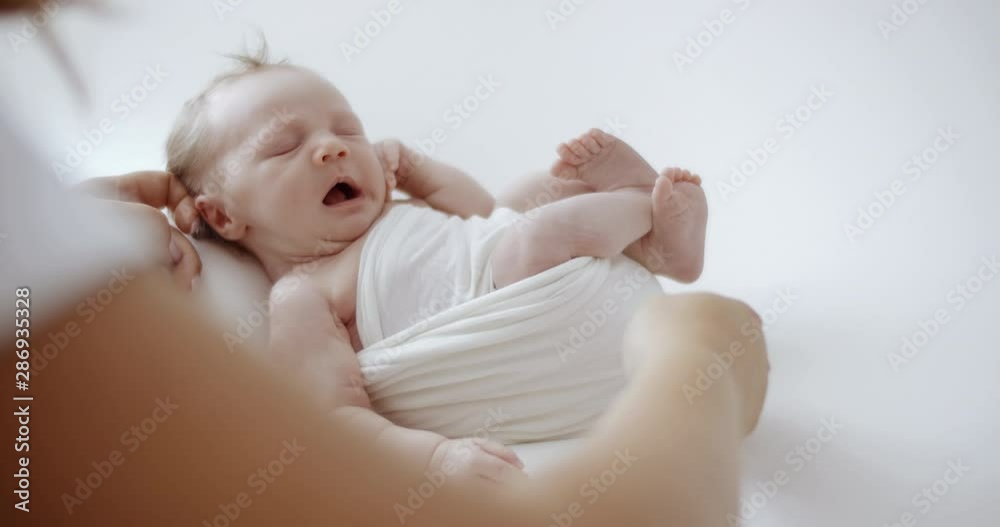 Cute newborn baby in white wrap sleeping on white blanket while mother’s arms holding her. RAW Graded footage 4K slow motion 50fps Cute newborn baby in white wrap sleeping on white blanket while mother’s arms holding her. RAW Graded footage 4K slow motion 50fps