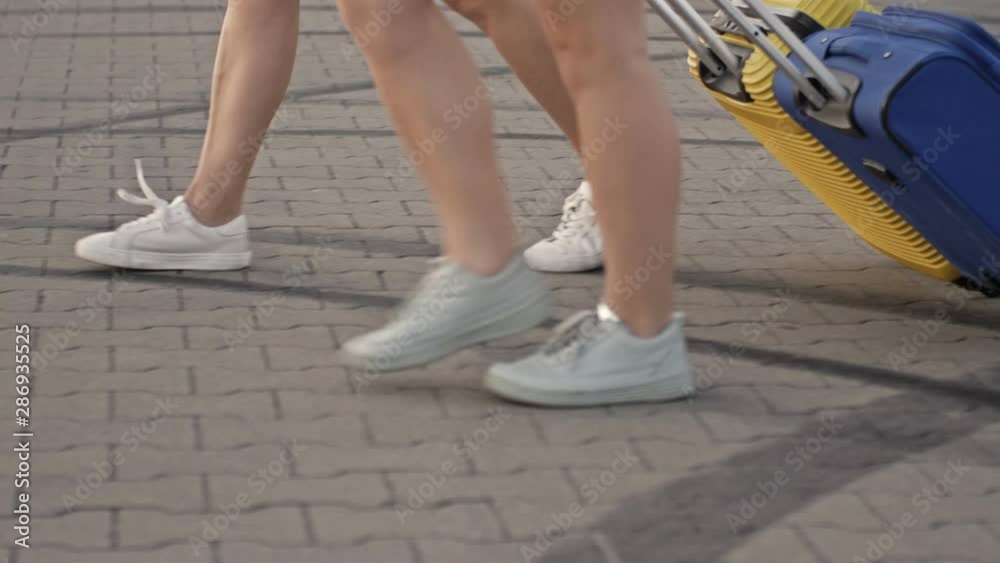 Travel on holiday vacation. Legs of two women rolling suitcases through courtyard. Female friends travelling together on holidays. Travel on holiday vacation. Legs of two women rolling suitcases through courtyard. Female friends travelling together on holidays.