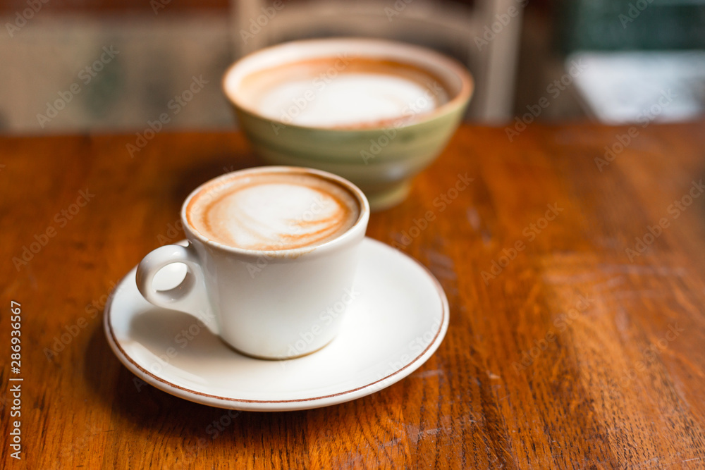 Two cups of cappuccino with latte art on wooden background. Concept of easy breakfast. Small and big ceramic cups Two cups of cappuccino with latte art on wooden background. Concept of easy breakfast. Small and big ceramic cups