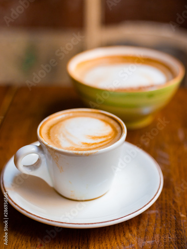 Two cups of cappuccino with latte art on wooden background. Concept of easy breakfast. Small and big ceramic cups
