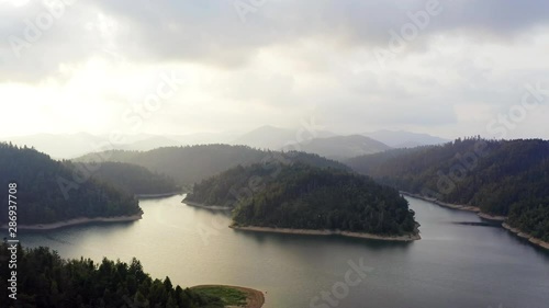 Aerial view of Lokve lake surrounded by hills and mountains with coniferous forest. Flying over the hill above the Lokve lake in Croatia. Nature background in 4K resolution.