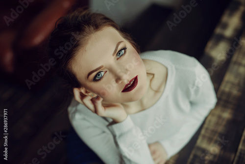 Portrait of young beutiful girl with brown curly hair, weared in white sweater,stylish makeup. Studio shot