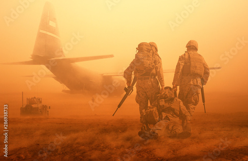 Fototapeta 2 soldiers helping wounded soldier between dust in battle field to board the hel