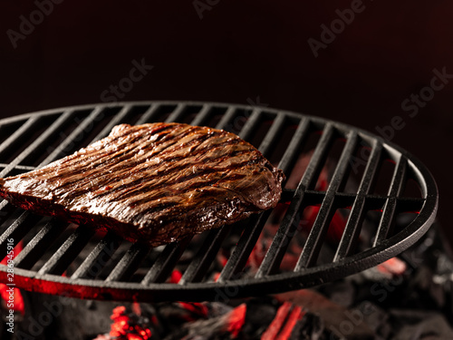 Cooking beef meat steak on hot grill barbecue with fire flams and smoke on black background.