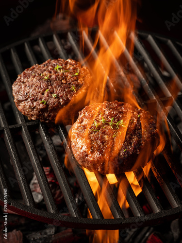 Grilling beef cutlet on hot grill barbecue grate with fire flams and smoke on black background.