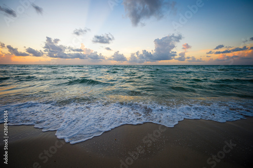 Fototapeta Naklejka Na Ścianę i Meble -  Bright scenic golden sunrise lighting up tropical clouds above gentle waves coming ashore