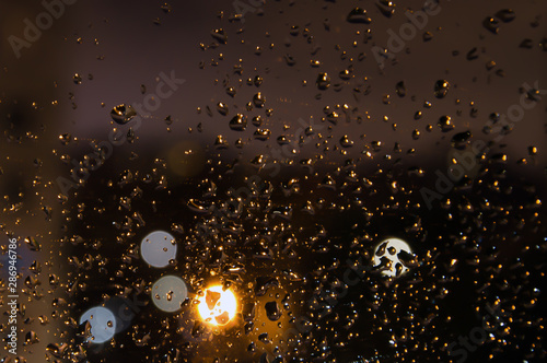 drops after rain on the glass of a home window in the late evening with a blurred background and bright lights