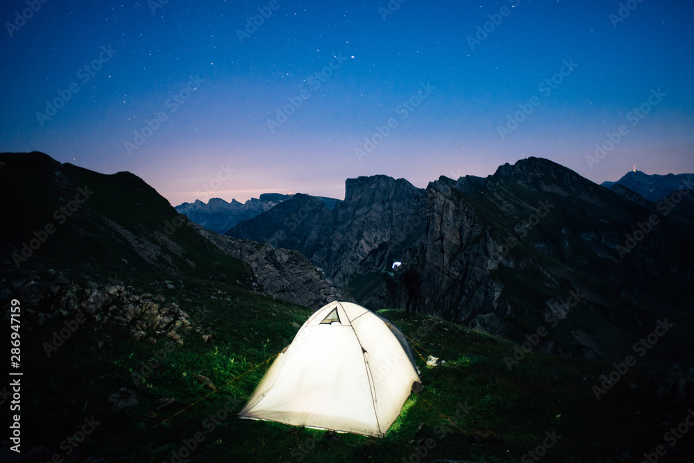 illuminated tent on a mountain ridge with stars in the background