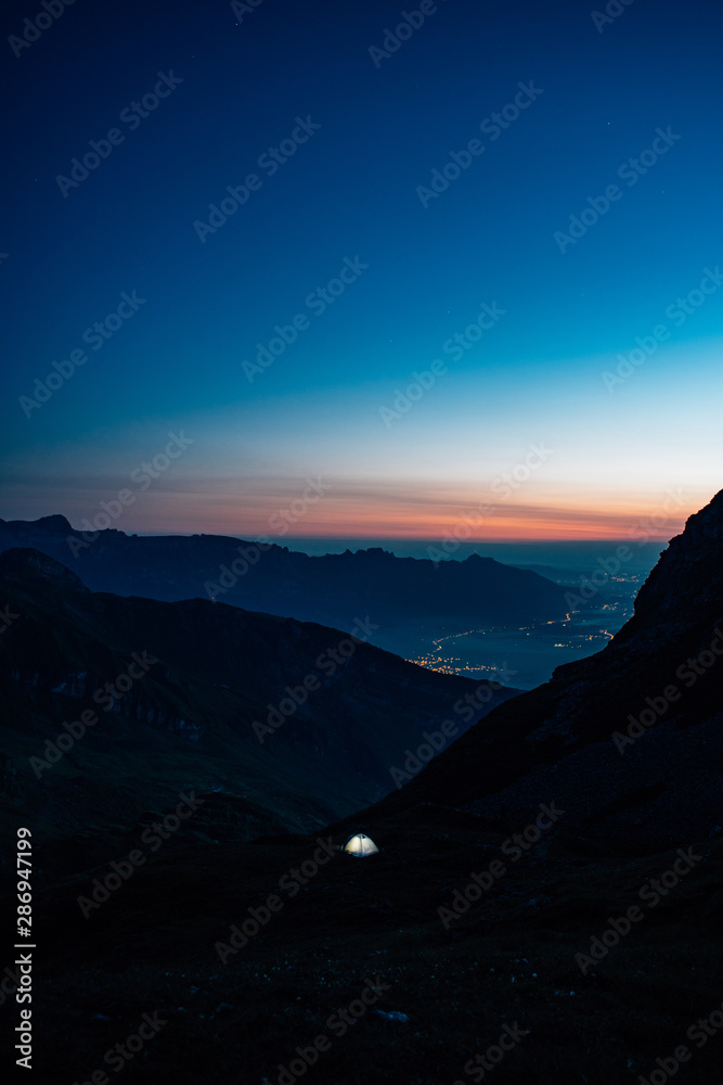 illuminated tent in the mountains with sunrise in the background