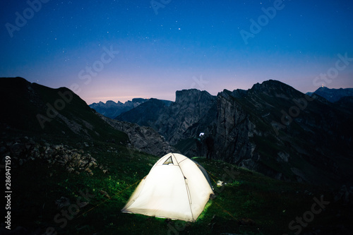 illuminated tent on a mountain ridge with stars in the background