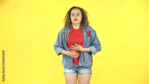 Cute female feels bad, her stomach hurts, feeling nausea on yellow background at studio photo