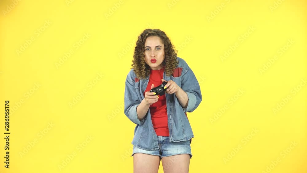 Young woman playing a video game using a wireless controller on yellow background Young woman playing a video game using a wireless controller on yellow background