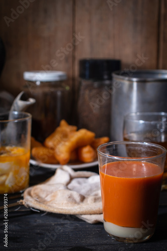Traditional Thai hot tea with milk on the wood table there are Traditional Thai hot coffee, deep-fried doughstick (patongko), hot tea and soft-boiled egg plated around.
