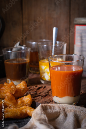 Traditional Thai hot tea with milk on the wood table there are Traditional Thai hot coffee, deep-fried doughstick (patongko), hot tea and soft-boiled egg plated around.