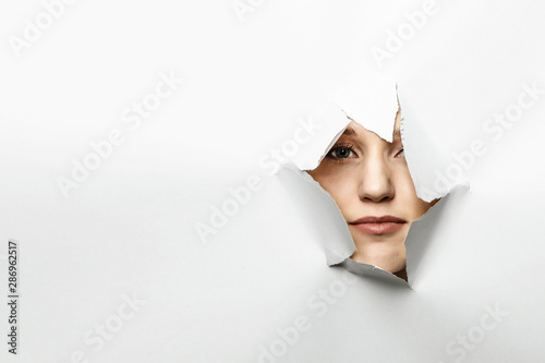 Woman looking out from a hole of torn paper © Sergey Nivens