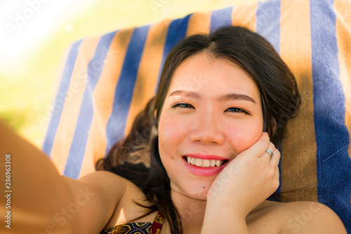 young beautiful and happy tourist Asian Korean woman taking selfie at tropical resort pool hammock smiling carefree and natural in Summer holidays getaway photo