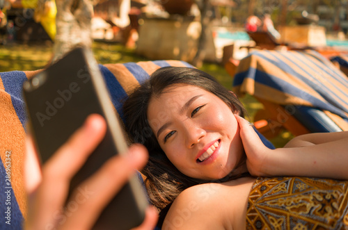 young beautiful and happy tourist Asian Korean woman taking selfie at tropical resort pool hammock smiling carefree and natural in Summer holidays getaway photo