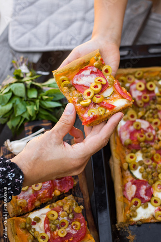 Homemade vegan pizza baked on tray. Square Italian vegetarian pizza with olives, tomatoes. Family eat food together. Hands of adult and child. © Viktor Kochetkov