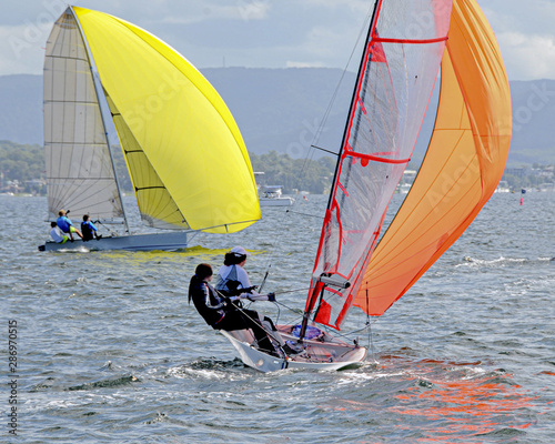 Children Sailing small sailboats with yellow and orange sails on an inland waterway.