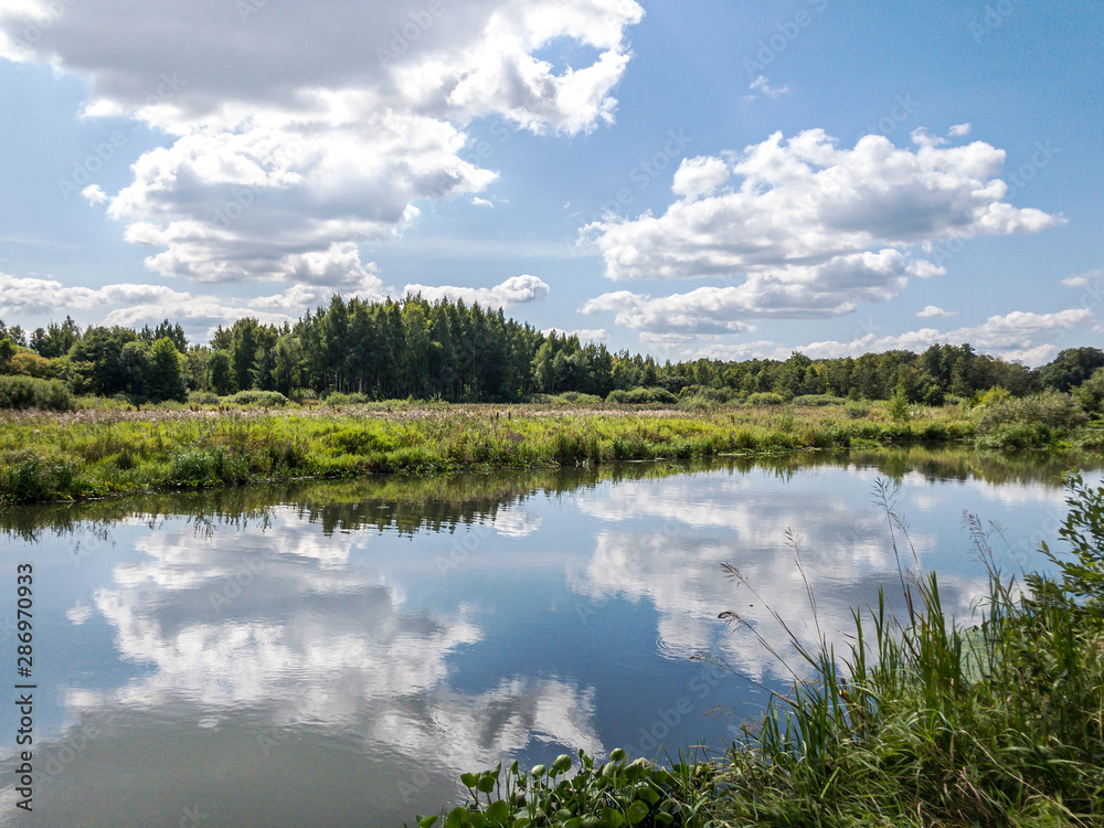 river in countryside in summer. cloudy sky reflected on water surface
