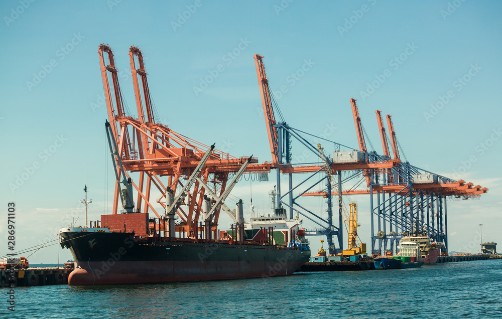 A cargo ship is loading with crane at Laemchabang port, Thailand. Logistics and transportation of Cargo ship with working crane bridge in blue sky background. Logistic import export and transport 