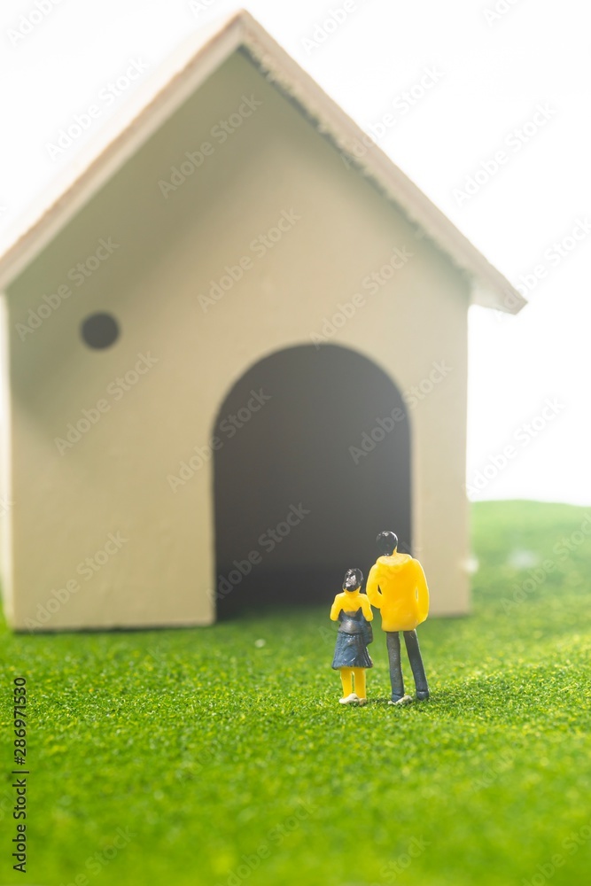 Miniature couple figures in front of a toy house, buying or owning a house concept Miniature couple figures in front of a toy house, buying or owning a house concept