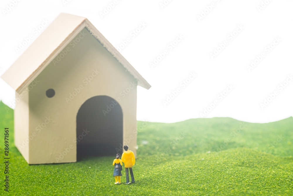 Miniature couple figures in front of a toy house, buying or owning a house concept Miniature couple figures in front of a toy house, buying or owning a house concept