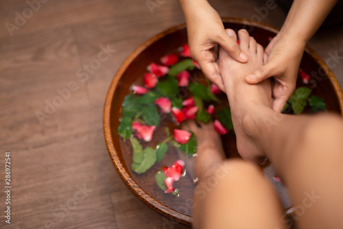 Top View  shot of a woman feet dipped in water with petals in a wooden bowl