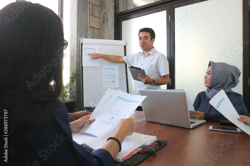 young professional male presentation at group meeting in white board with tablet and laptop, office meeting group