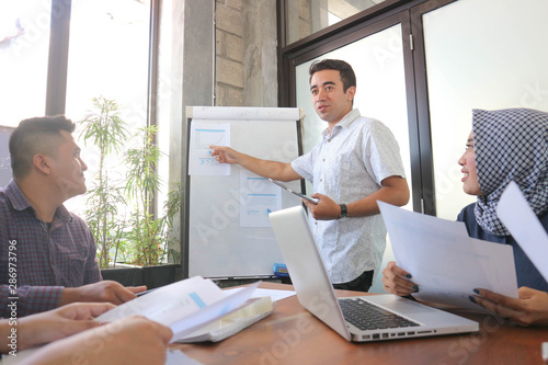 young professional male presentation at group meeting in white board with tablet and laptop, office meeting group