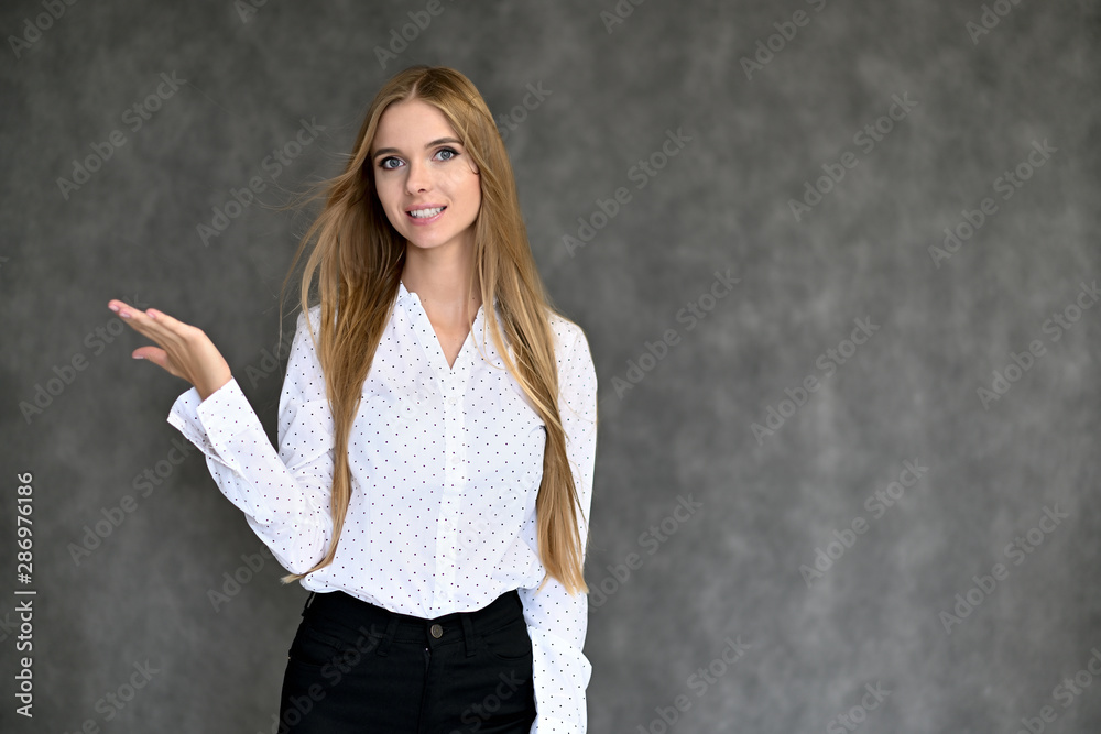 Portrait of a beautiful pretty girl student in a white shirt with long curly hair on a gray background. Beauty and brightness. Shows hands to the side, smiles with different emotions. Portrait of a beautiful pretty girl student in a white shirt with long curly hair on a gray background. Beauty and brightness. Shows hands to the side, smiles with different emotions.