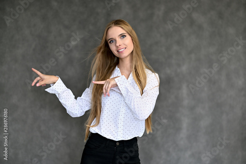 Portrait of a beautiful pretty girl student in a white shirt with long curly hair on a gray background. Beauty and brightness. Shows hands to the side, smiles with different emotions.