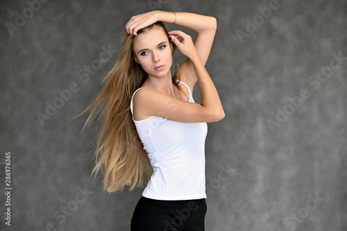 Portrait of a beautiful pretty girl student in a white T-shirt with long curly hair on a gray background. Beauty and brightness. Shows hands to the side, smiles with different emotions.