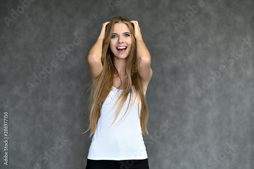 Portrait of a beautiful pretty girl student in a white T-shirt with long curly hair on a gray background. Beauty and brightness. Shows hands to the side, smiles with different emotions.