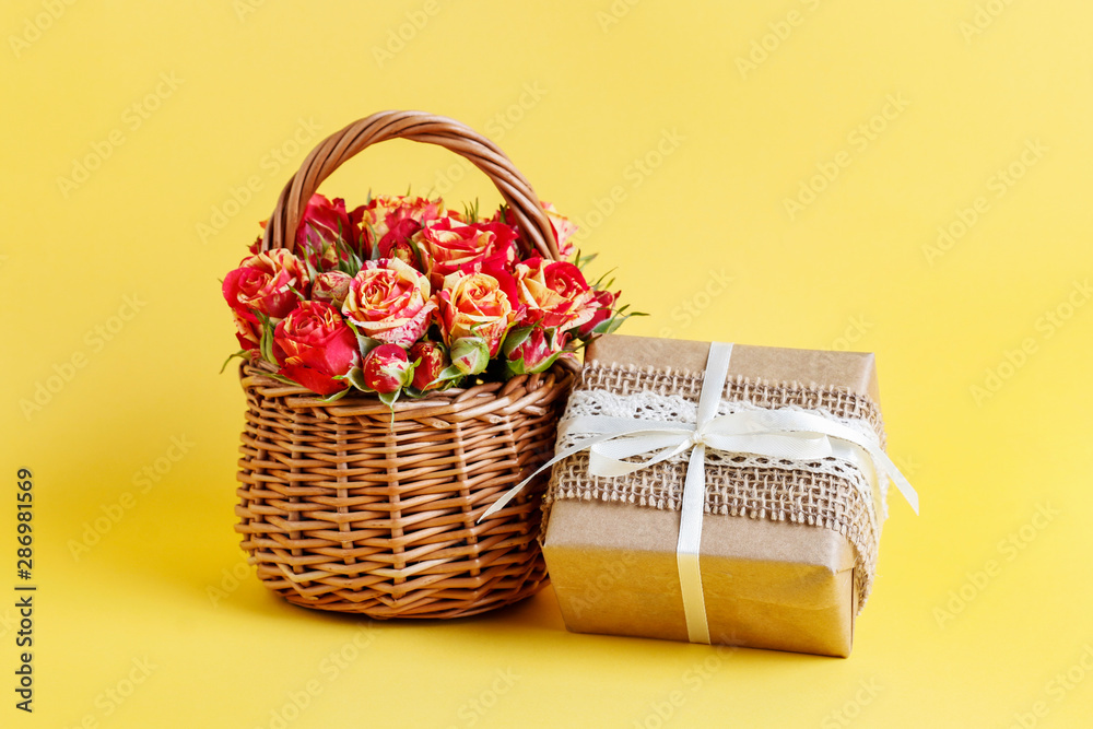 Wicker basket with roses and beautifully wrapped gifts on yellow background. Wicker basket with roses and beautifully wrapped gifts on yellow background.