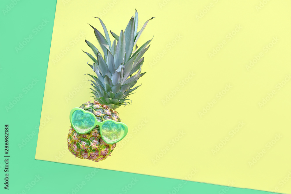 Funny pineapple in heart-shaped sunglasses on geometric diagonal paper background in neo green and yellow