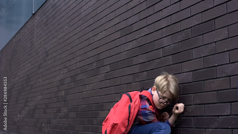 Scared schoolboy leaning against wall, hiding from bullying, intimidation Scared schoolboy leaning against wall, hiding from bullying, intimidation