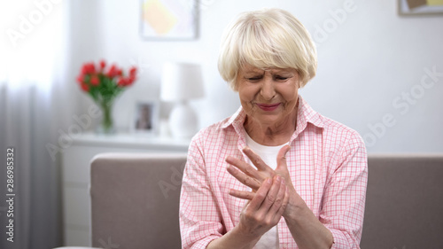 Upset old woman suddenly feeling sharp pain in wrist, arthritis health problem photo