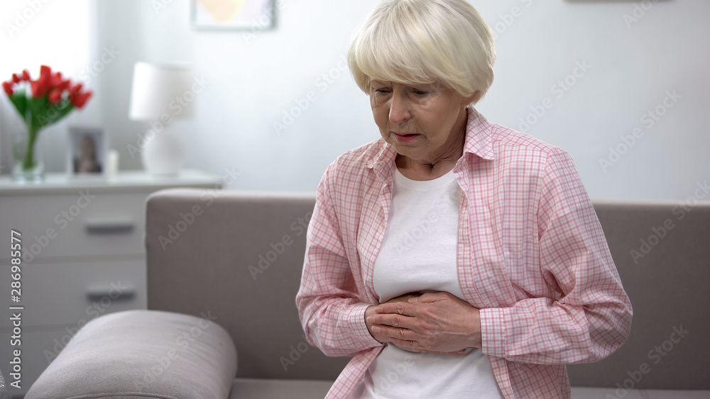 Upset old woman holding hands on stomach, suffering from gastritis disease Upset old woman holding hands on stomach, suffering from gastritis disease