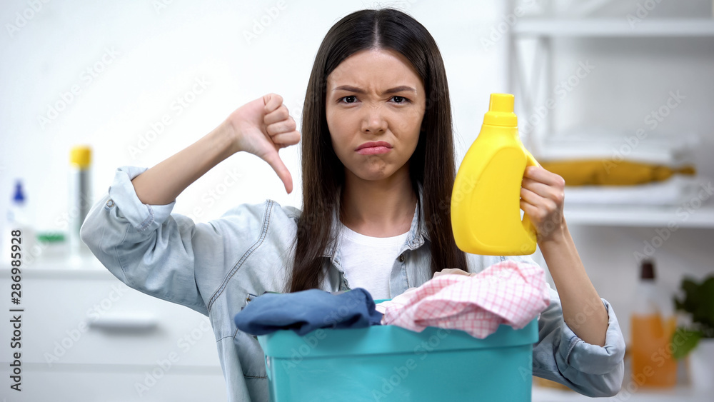 Woman with basket full of clothes and laundry detergent showing thumbs-down Woman with basket full of clothes and laundry detergent showing thumbs-down