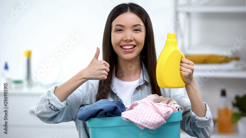 Housewife with basket full of clothes and laundry detergent showing thumbs-up