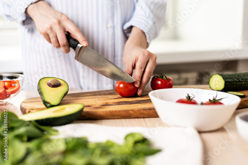 female hands with knife in the kitchen, slicing red tomato for salad