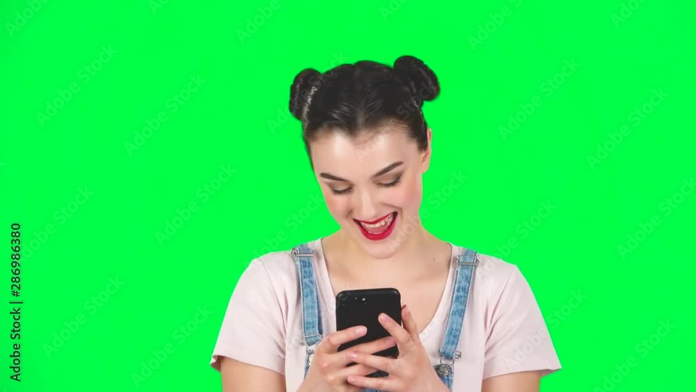 Young smiling woman texting on her phone on green screen, slow motion Young smiling woman texting on her phone on green screen, slow motion