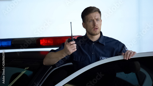 Worried policeman calling for help on two-way radio in patrol car, offence, law