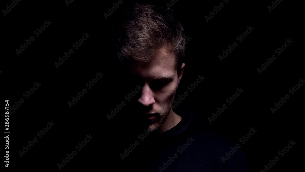 Man looking down against black background, feeling guilty for committed crime - obrazy, fototapety, plakaty 