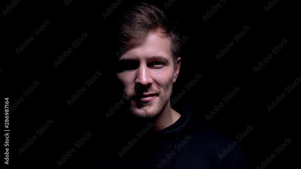 Fototapeta premium Dangerous man with crazy grin looking into camera maniac against dark background