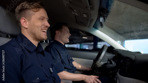 Cheerful police mates laughing in patrol car during daily duty, friendship