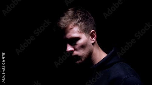 Depressed man standing against black background, suffering pain of relative loss